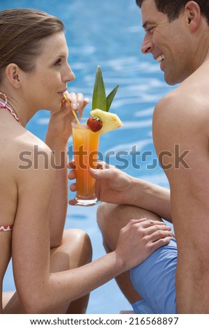 Couple sharing tropical drink at poolside