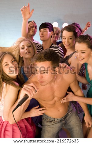 People dancing behind bare chested man singing into microphone