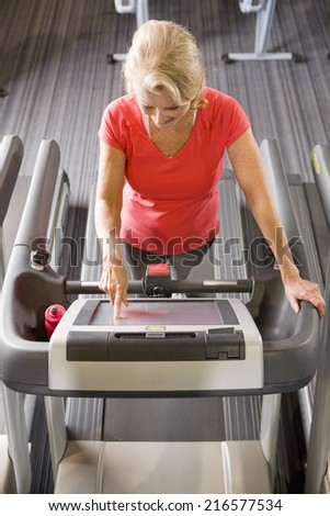 Senior woman programming treadmill in health club