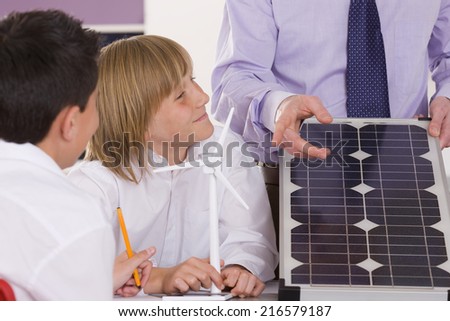 Students listening to teacher explaining solar panel and wind turbines in classroom