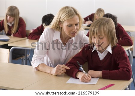 Teacher helping school boy with test in classroom