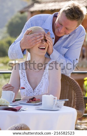 Man covering woman\'s eyes on cafe patio