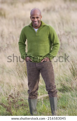 Smiling man standing in field with hands in pockets