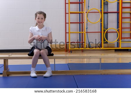 School girl sitting on bench and holding ball in school gymnasium