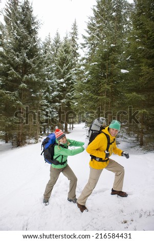 Woman pushing man with backpack up snowy slope in woods