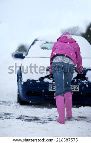Woman pushing snow covered car in snowfall