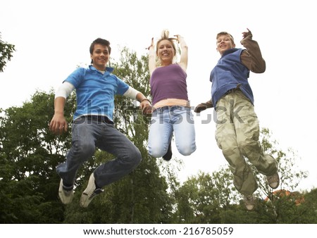 Teenage boys and girl jumping in a park.