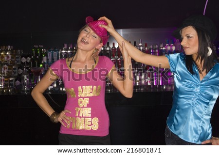 Young woman taking a woman's hat off in a nightclub