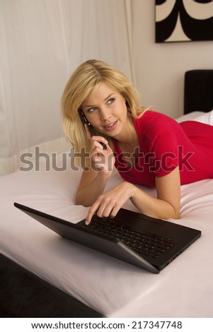 High angle view of a young woman lying in front of a laptop and talking on a flip phone