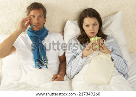 Portrait of a mid adult woman reclining with a mid adult man on the bed and drinking a cup of tea