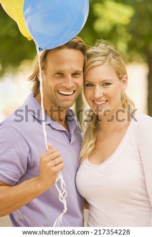 Portrait of a young man holding balloons and a young woman standing beside him