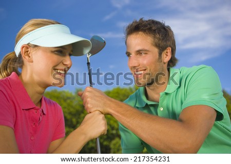 Close-up of a mid adult couple holding a golf club and smiling