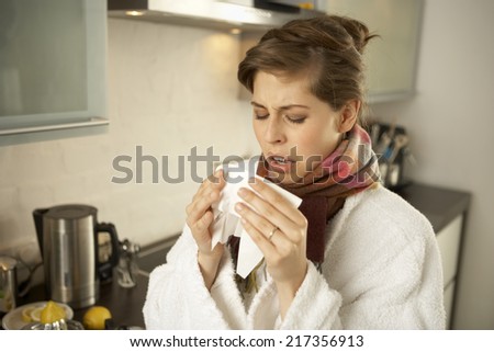 Close-up of a mid adult woman sneezing in the kitchen
