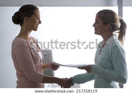 Side profile of two businesswomen shaking hands and smiling