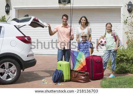 Portrait of smiling family packing car in sunny driveway