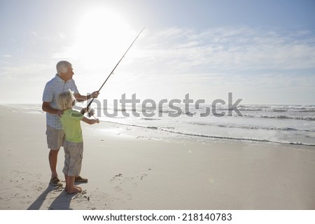 Grandfather and grandson with fishing rod on sunny beach