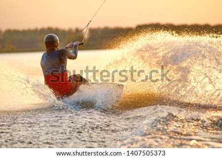 Wakeboarder making tricks. Low angle shot of man wakeboarding on a lake. Man water skiing at sunset. Stock fotó © 