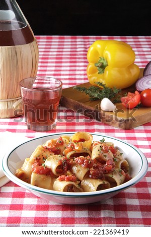 table set with plate of pasta with tomato sauce, bottle of wine, peppers, onion and garlic on gingham tablecloth at an Italian eatery