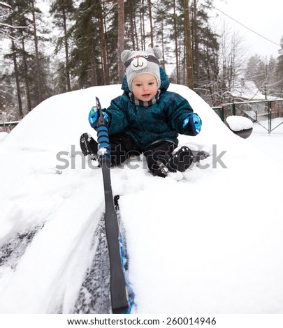 Funny baby boy cleans car bonnet from snow