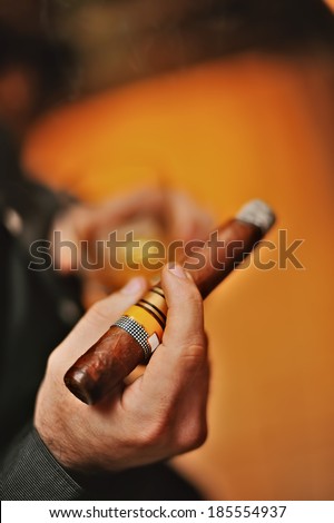 man\'s hand with a cigar on a glass of whiskey background