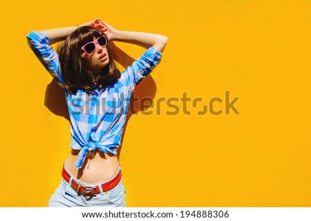portrait of a beautiful bright blue shirt girl with glasses on a background of orange walls and blue sky