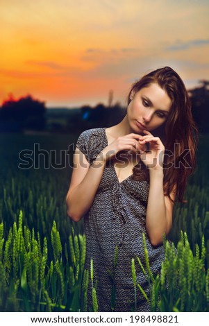 portrait of beautiful young woman standing in green field at sunset outdoor