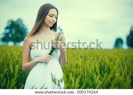 portrait of young woman standing on a wheat field with sunrise on the background