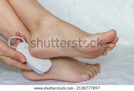 close up of woman's heels holding a pumice stone, with brush on the other side. natural gray pumice stone for feet. care for dry heels and feet. tools for feet care. ストックフォト © 