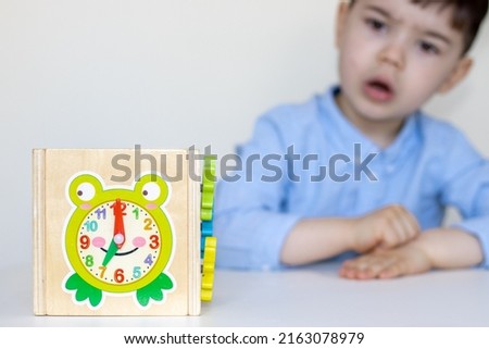 cute little boy expressing wow, shocked amazed face, open mouth and looking at 7 o'clock. wooden toy cube with frog drawn shows time,kid sitting on white desk.preschool boy,back to school Foto stock © 