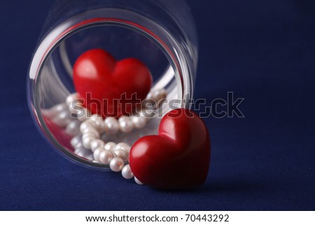 Love in jar. Pair of hearts and pearl necklace in a glass jar. Shallow depth with focus in near heart and pearls. Isolated on blue background.