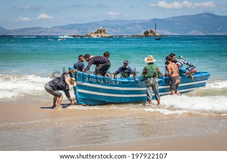 JUNE 8.2014-TANGIER, MOROCCO:  fishing boat at the beach and other men  help put the boat in the sand