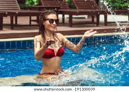 Outdoor fashion portrait of young sexy woman having fun at the pool and makes water splash.
