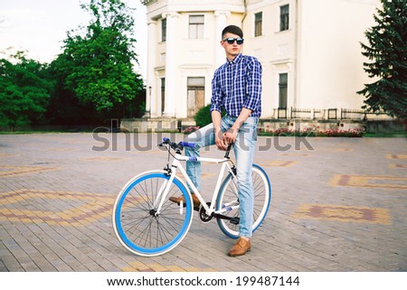 Outdoor fashion portrait of young hipster stylish man riding his bike at old town, and enjoy warm weather.
