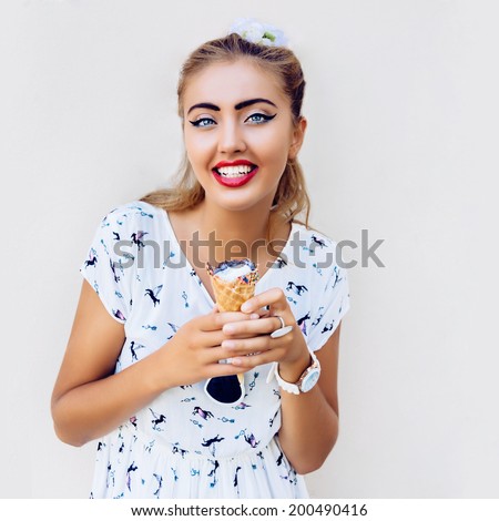 Fashion portrait of young pretty woman with big happy smile, holding big bright ice cream in her hands, laughing and having fun near beige wall, not isolated.