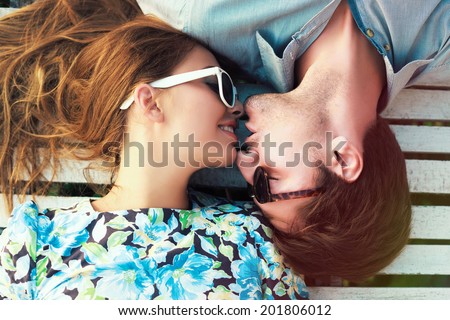 Happy young couple laying on white floor and have a sweet kiss, wearing retro clothes and sunglasses.