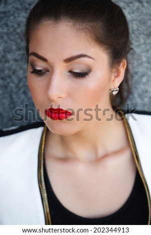 Close up fashion portrait of female model with bright make au and simple black and white outfit, posing in the front of grey wall.