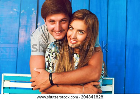 Young pretty blonde girl and handsome man hugs at blue background, having great time at their romantic date, wearing color matching blue outfits.