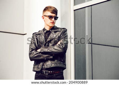 Fashion portrait of young handsome brutal stylish man in trendy leather jacket with spikes posing at urban background.