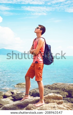 Handsome stylish hipster man standing alone at beautiful exotic neck in hot summer day. View on beautiful clear blue ocean water.