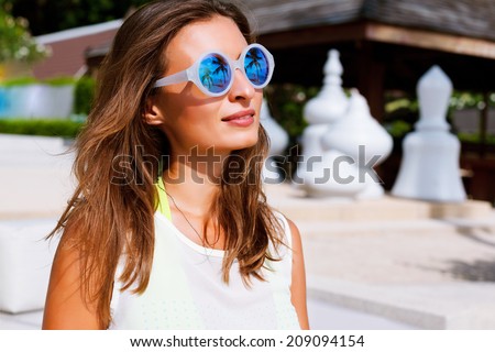 Close up fashion portrait of beautiful brunette girl with perfect bronze skin, wearing trendy round mirrored sunglasses, light background.