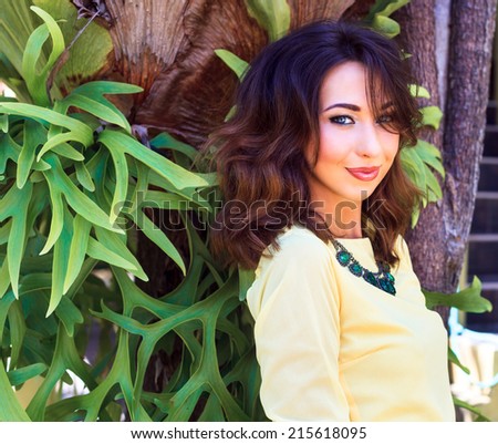 Close up fashion portrait of sensual beautiful brunette woman with bright make up, posing at exotic garden near beautiful fantastic tree, wearing blouse and big necklace. Have trendy hairstyle.