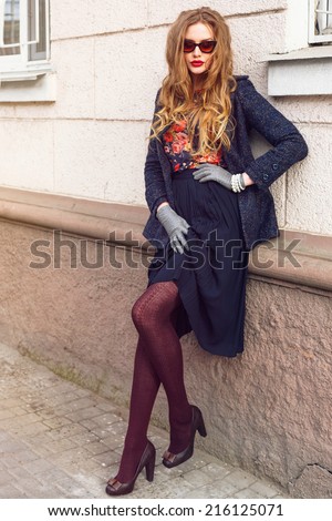 Fashion portrait of young sexy woman posing at the street at trendy coat long skirt and hight heels shoes, have vintage sunglasses, and hairstyle. Autumn retro style.