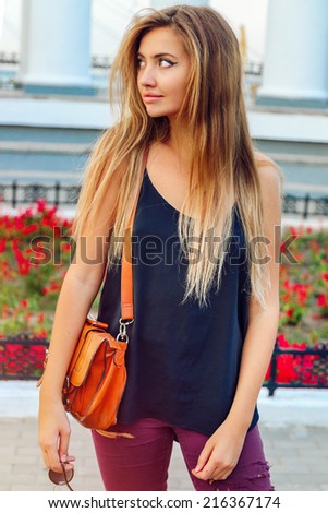 Young pretty woman walking alone at nice sunny day, white city background. Have long trendy blonde ombre hairs,