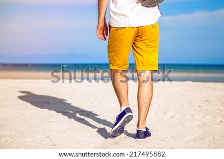 Fashion outdoor image of stylish man walking alone at beautiful beach, enjoy freedom and nice relaxed vacation day near ocean.