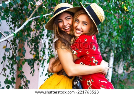 Two happy pretty young sisters, hugs smiling laughing  and having funny crazy time together, bearing stylish retro vintage feminine clothes and hats. Outdoors.