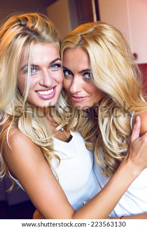 Indoor lifestyle fashion portrait of two pretty positive emotional young blonde girls, two sisters hugs on kitchen in the morning.