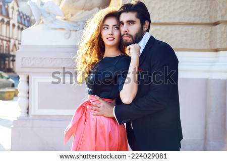 Young beautiful sexy couple hugs on the street, enjoy their romantic date, spend nice time together, posing on the street at classic glamour trendy evening clothes. Bright sunny colors.