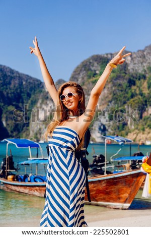 Outdoor lifestyle portrait of happy girl, put her hands to the air and enjoy her vacation in hot tropical Phi Phi island, amazing view on local boats and mountains. Fashion portrait of young traveler.