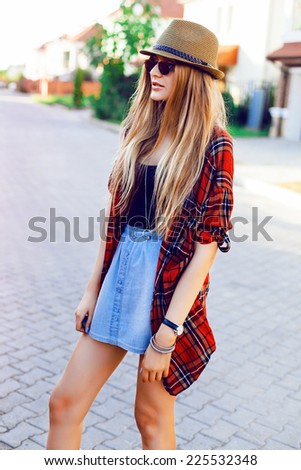 Young pretty blonde hipster girl posing on the street, wearing plaid shirt, mini denim skirt, hat and sunglasses, urban style.