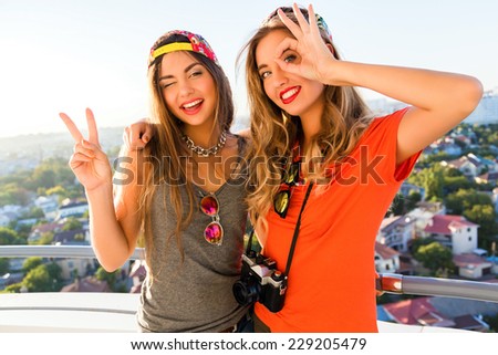 Two pretty best friend cheerful girls having fun and making funny crazy faces at the roof, amazing view on the city, bright colors.
